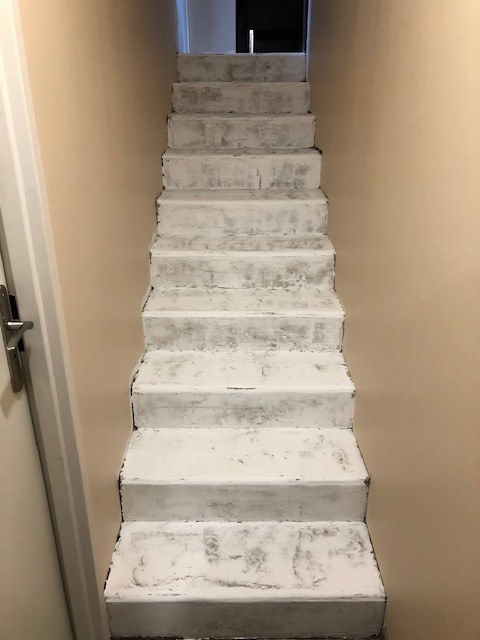 Escalier intérieur en cours de reprise : marches et contremarches enduites, surface encore claire et irrégulière.