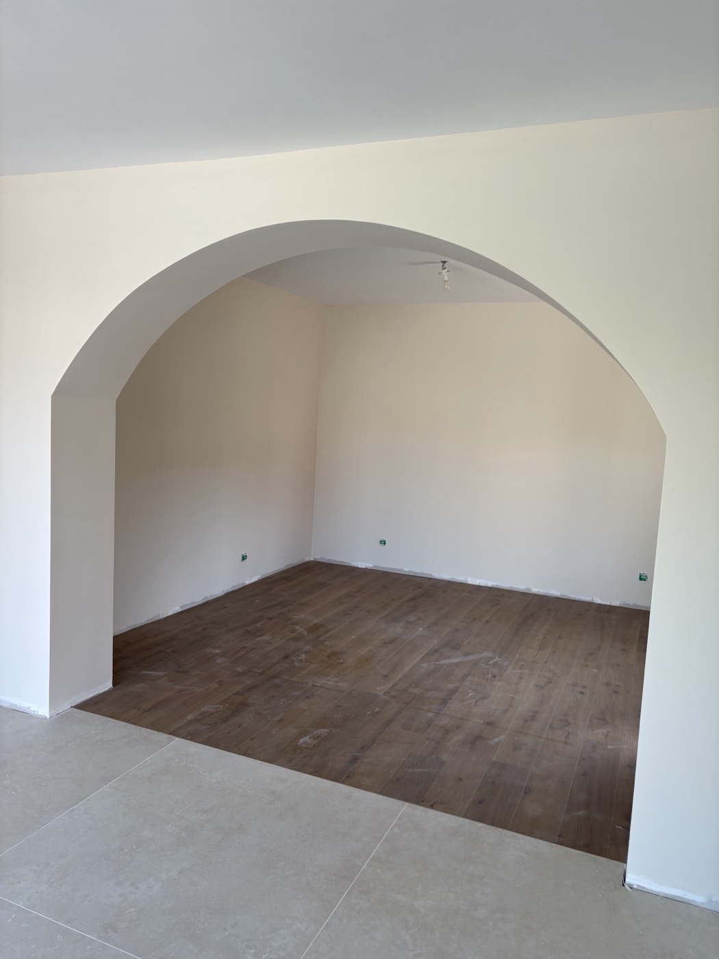 Arche en plâtre lissée ouvrant sur une pièce au parquet.