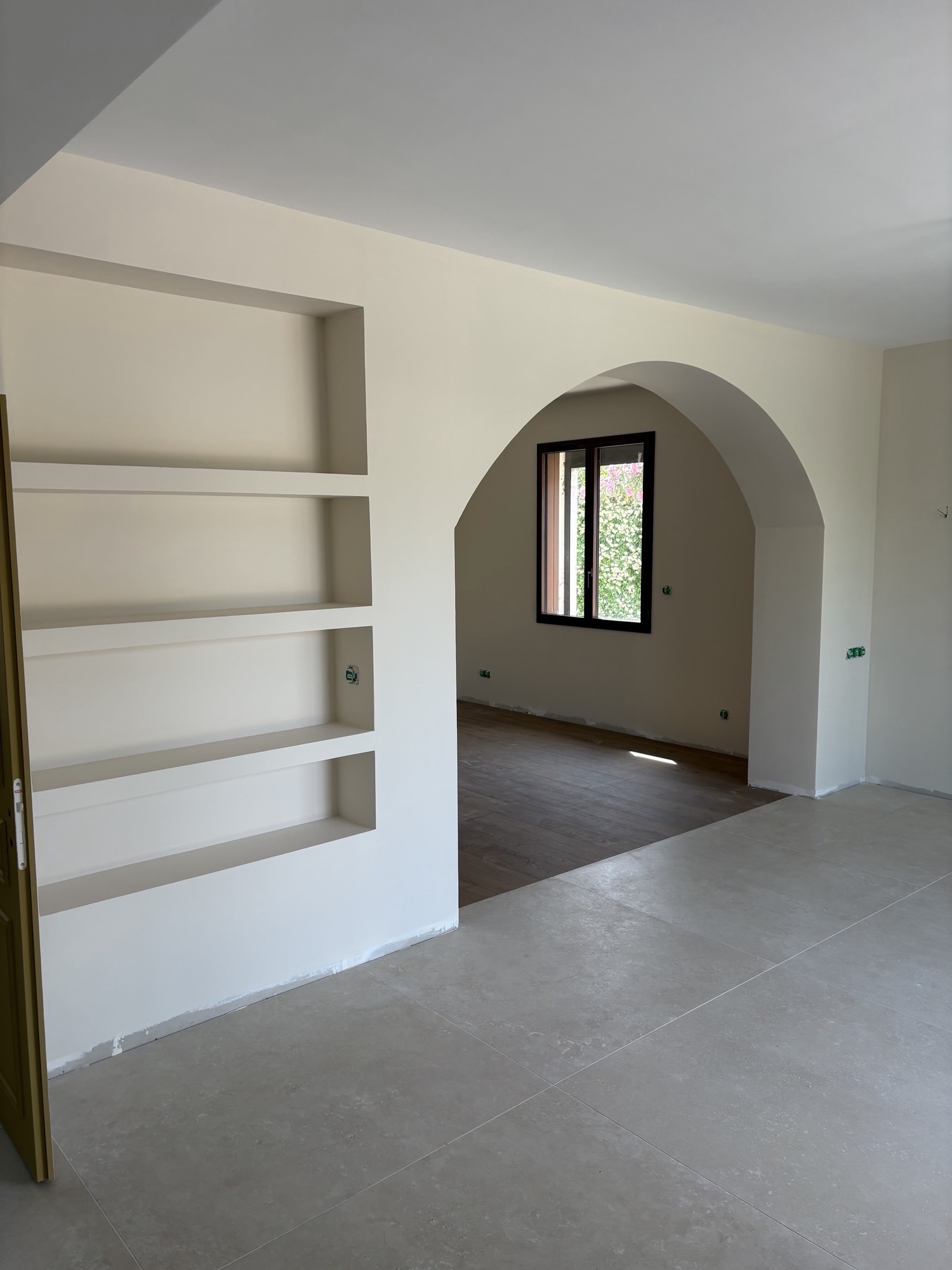 Séjour rénové à Saint-Martin-de-Crau : bibliothèque en niches de placo et arche maçonnée, murs enduits et peints.