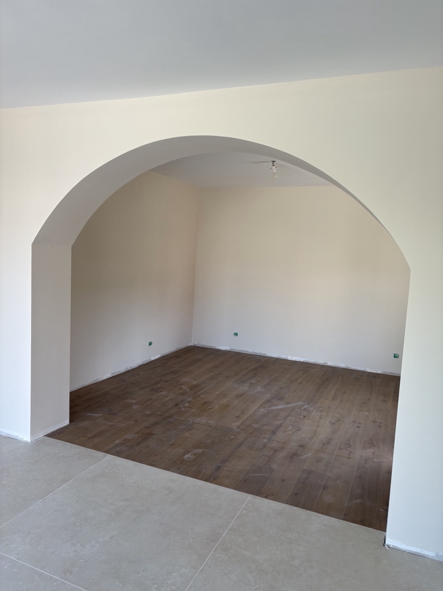 Arche en plâtre ouvrant sur une pièce au parquet, finition lisse.