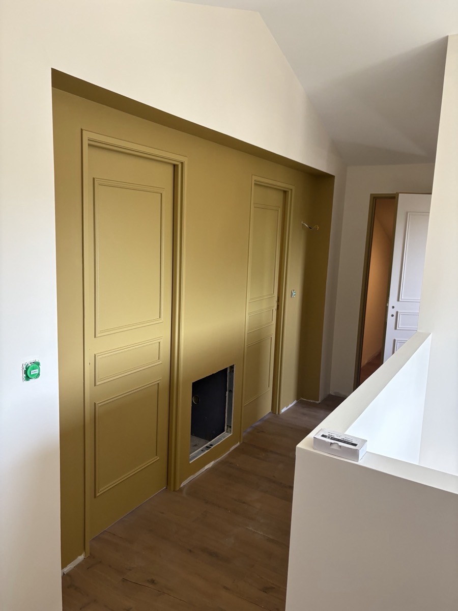 Portes et mur peints en ocre moutarde, découpes nettes le long du plafond.